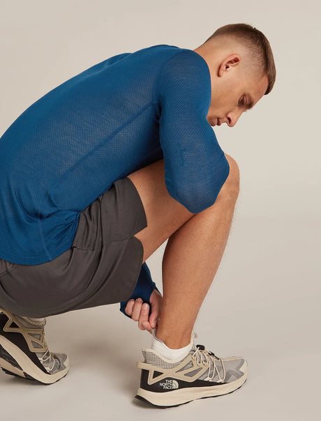 A man in a blue long-sleeve athletic mesh shirt and gray shorts crouches while tying the laces of his gray and white running shoes. The brand 'The North Face' is visible on the shoe heel. - Icebreaker Merino Multisport Light Micro Socks (Men's) - Ecru Heather/Alloy/Snow