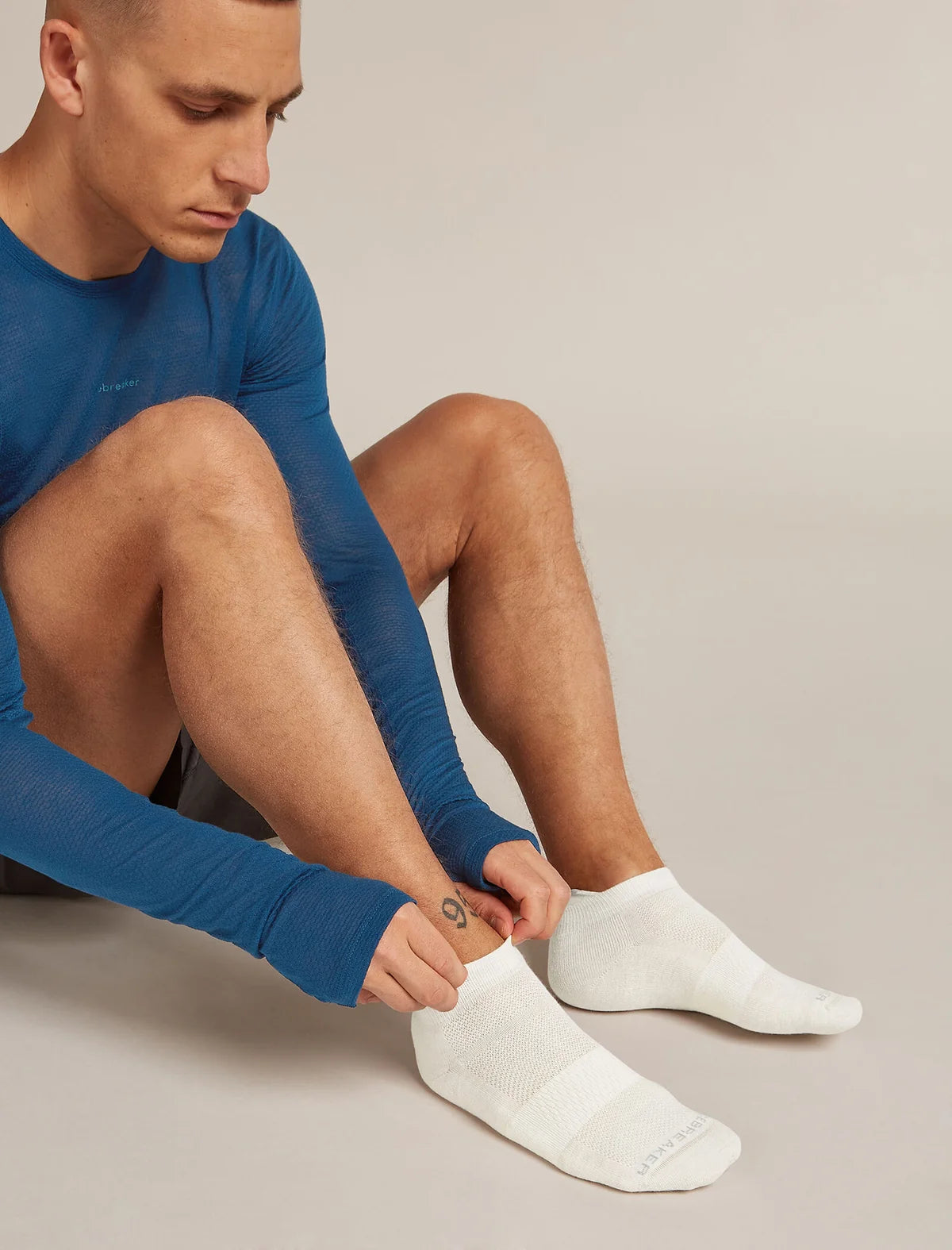 Man wearing blue long-sleeve shirt and white socks sitting on a neutral background - Icebreaker Merino Multisport Light Micro Socks (Men's) - Ecru Heather/Alloy/Snow