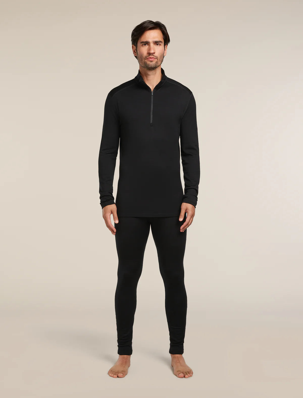 Man wearing a black long-sleeve top and pants on a beige background - Icebreaker Merino 260 Tech Long Sleeve Half Zip (Men's) - Black