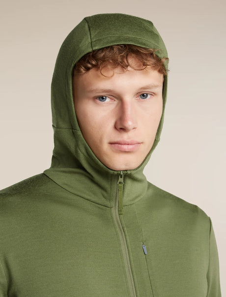 A close-up of a man wearing an olive green hooded zip-up fleece jacket against a solid beige background. - Icebreaker Merino 260 Quantum Long Sleeve Zip Hoodie (Men's) - Sphagnum