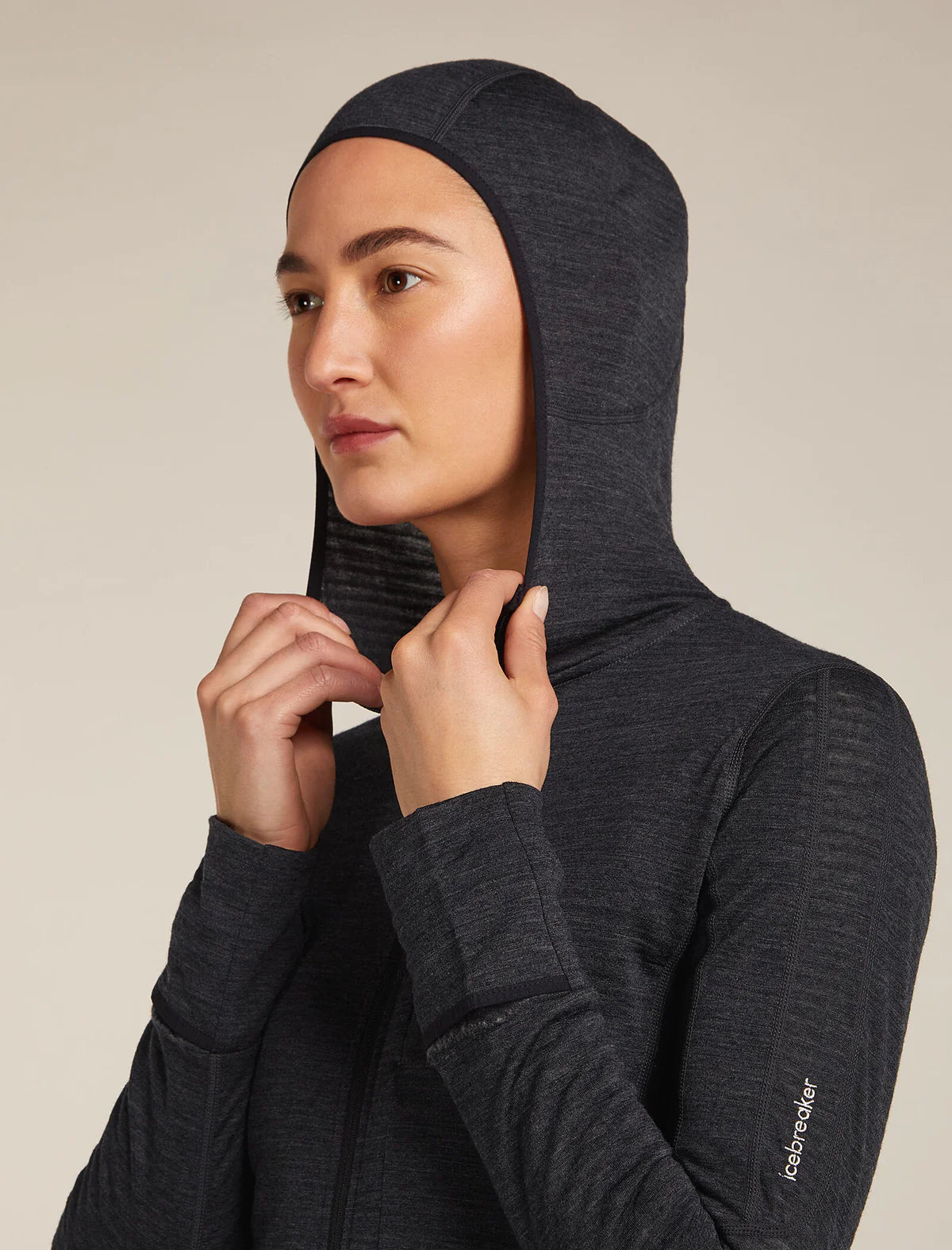 Person wearing a dark gray hooded jacket with a visible brand logo on a beige background - Icebreaker Merino Blend 200 Realfleece Descender Long Sleeve Zip Hoodie (Women's) - Jet Heather/Black