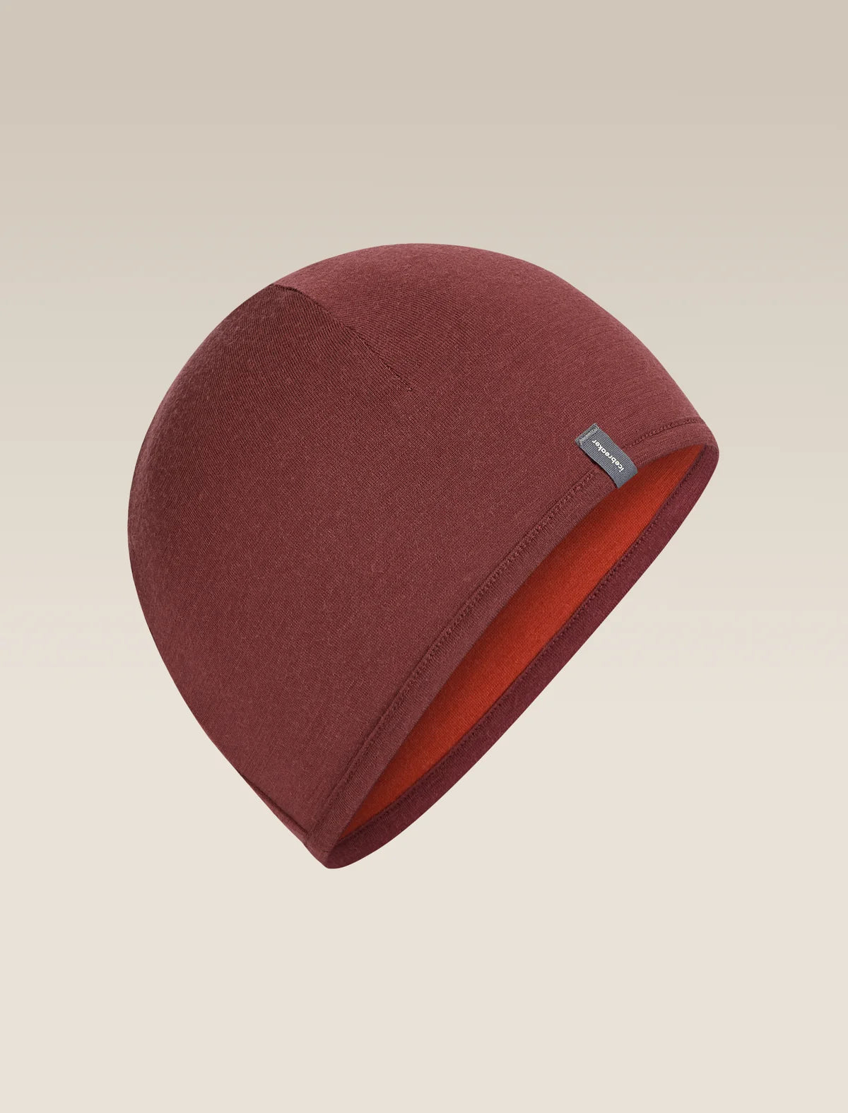 A dark red knit beanie hat with a small gray brand tag on the side, displayed against a light beige gradient background. - Icebreaker Merino 200 Pocket Hat (Unisex) - Agate/Port