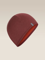 A dark red knit beanie hat with a small gray brand tag on the side, displayed against a light beige gradient background. - Icebreaker Merino 200 Pocket Hat (Unisex) - Agate/Port