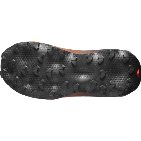 The black treaded outsole of a trail running shoe, showing its aggressive grip pattern and textured design against a white background. - Salomon Ultra Glide 4 Shoes (Women's) - Huckleberry/Black/Red Orange