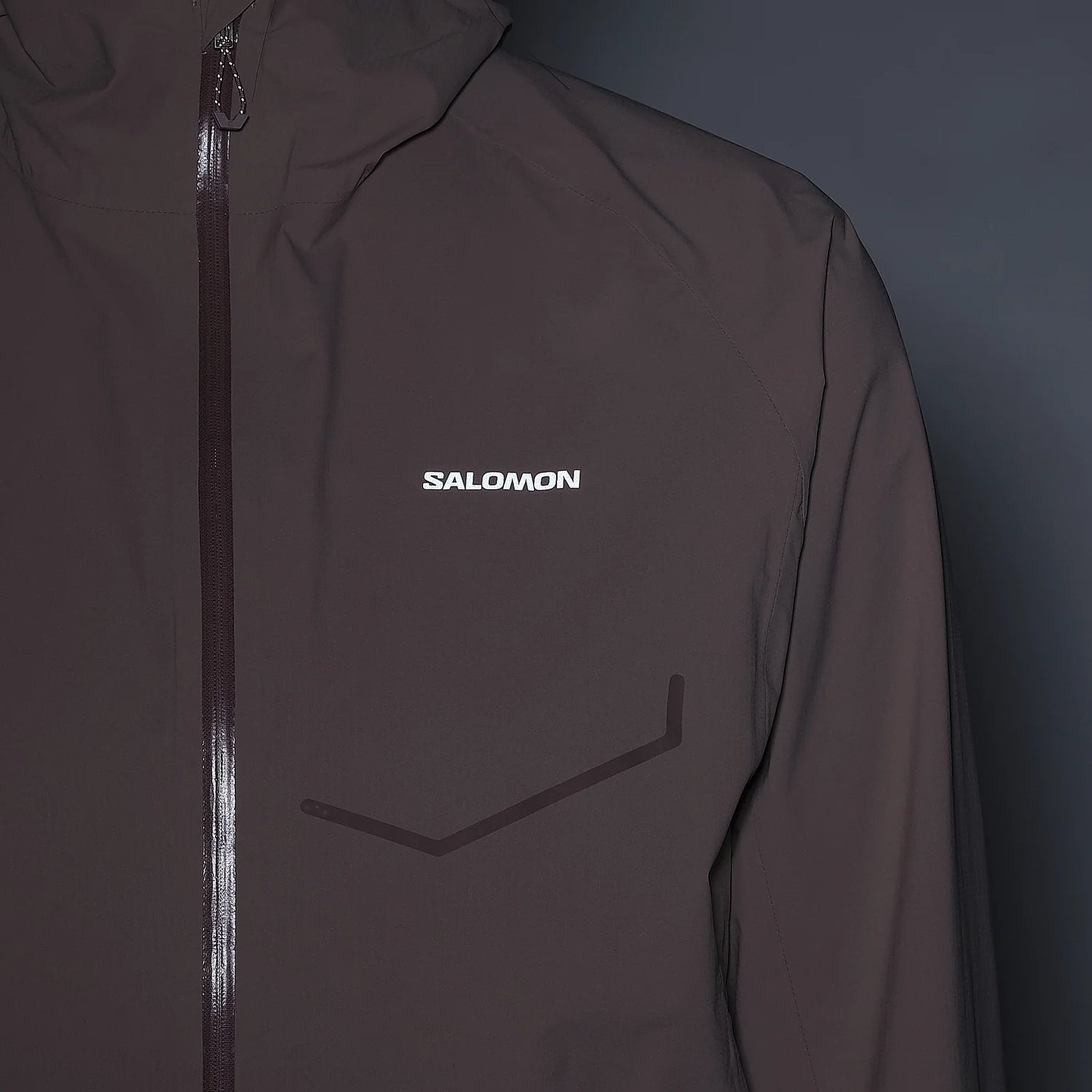 A close-up of a Salomon jacket in a dark taupe-brown color, featuring a white Salomon logo on the left chest and a dark reflective chevron detail on the front. - Salomon Bonatti Waterproof Jacket (Women's) - Antler