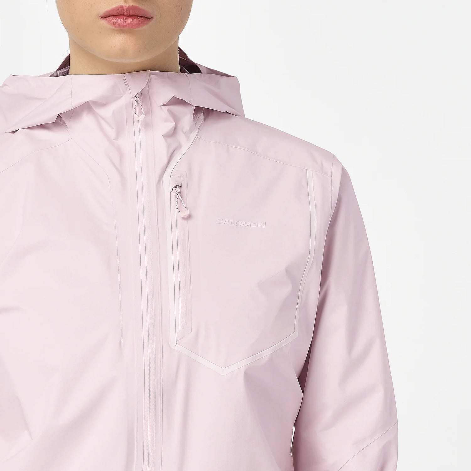 A close-up of a person wearing a light pink hooded jacket with a front zipper and a zippered chest pocket. The brand name 'balmy' is subtly printed in white on the chest pocket. - Salomon Bonatti Pro Jacket (Women's) - Icy Pink