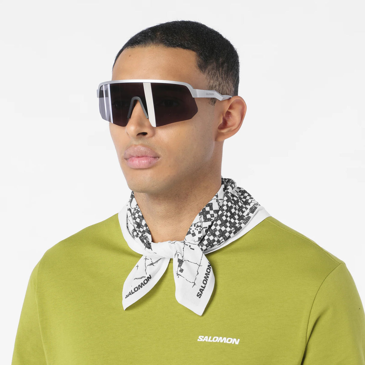 Man wearing a green shirt, white sunglasses, and a Salomon bandana on a white background - Salomon Bandana Graphic (Unisex) - Whisper White/Deep Black