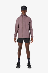 A male model wearing a dusty rose zip-up hooded jacket with a vertical white 'ROCKNROLLER' logo on the chest, black running shorts, a black cap, and black running shoes, standing against a light gray background. - NNormal Trail Rain Jacket 02 (Men's) - Purple