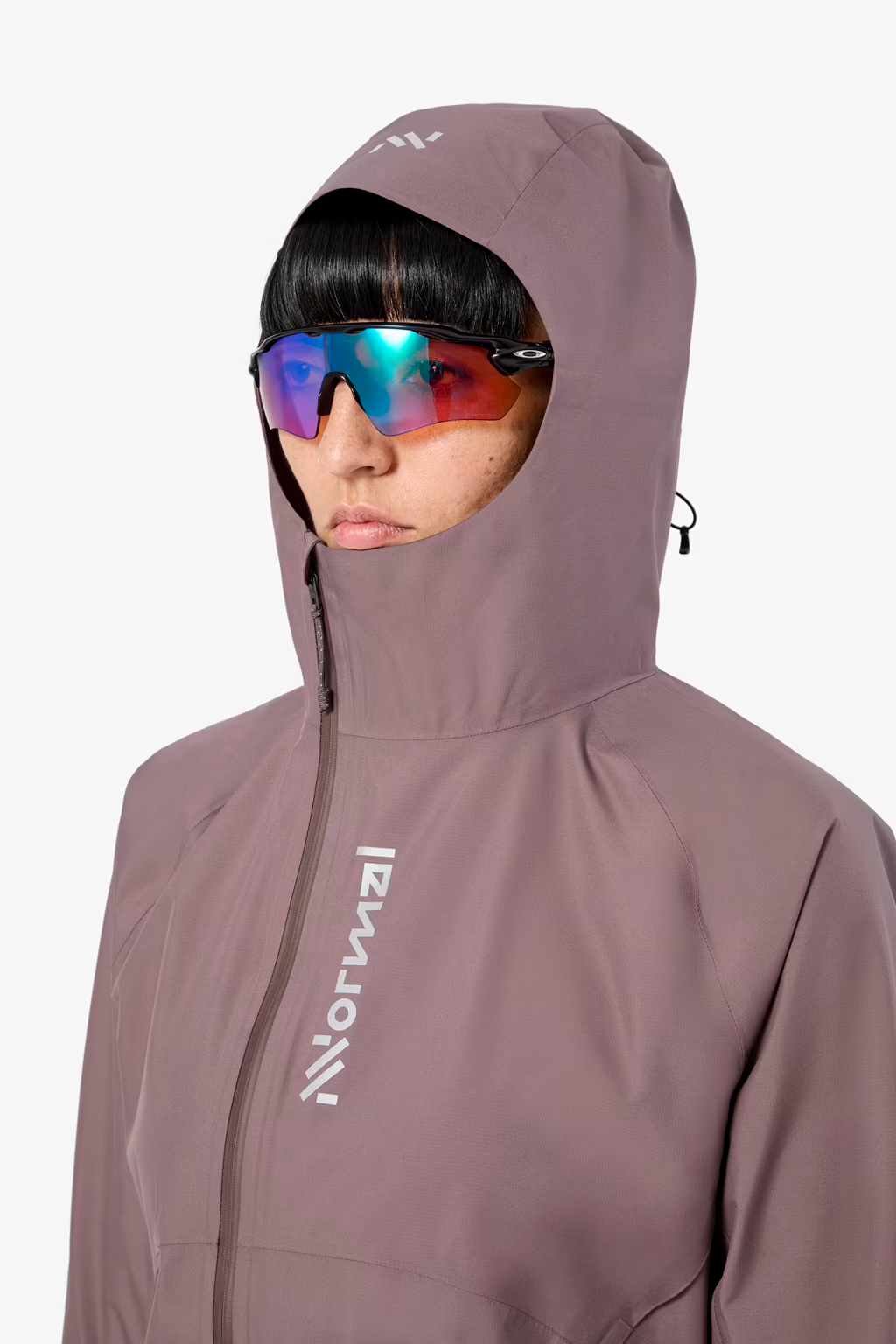 A close-up of a person wearing a muted mauve-pink hooded jacket with a white vertical Norrøna logo on the chest and a white logo on the hood. The person is also wearing mirrored ski sunglasses against a clean white background. - NNormal Trail Rain Jacket 02 (Women's) - Purple