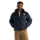 A man wearing a navy blue and black puffer jacket with a white embroidered The North Face logo on the chest, paired with tan pants, against a solid white background. - The North Face 1996 Retro Nuptse Jacket (Men's) - Summit Navy/TNF Black