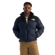 A man wearing a navy blue and black puffer jacket with a white embroidered The North Face logo on the chest, paired with tan pants, against a solid white background. - The North Face 1996 Retro Nuptse Jacket (Men's) - Summit Navy/TNF Black