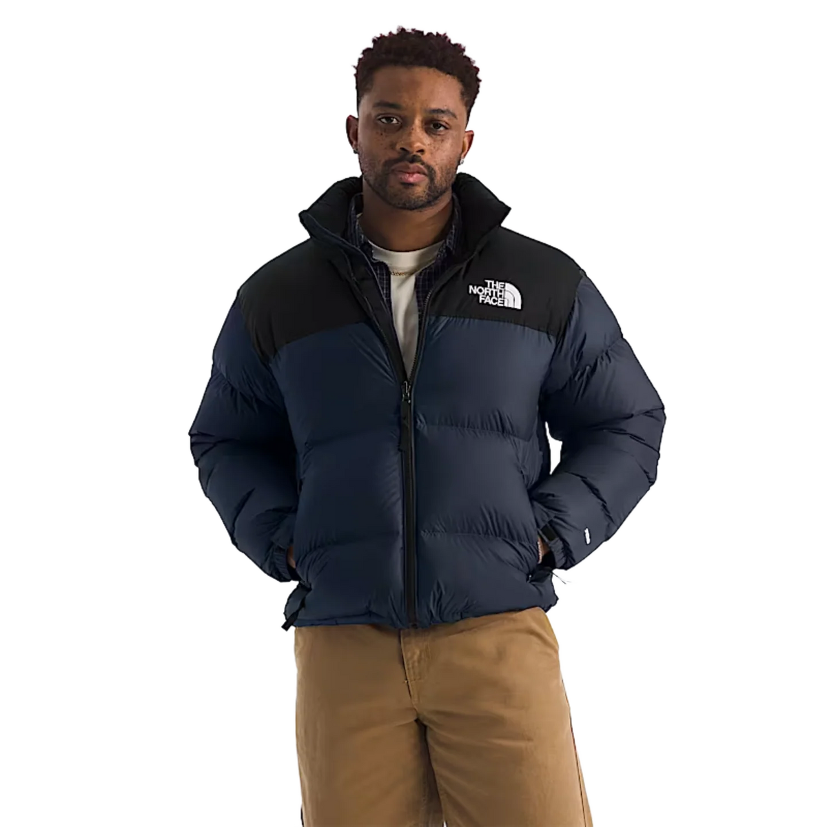 A man wearing a navy blue and black puffer jacket with a white embroidered The North Face logo on the chest, paired with tan pants, against a solid white background. - The North Face 1996 Retro Nuptse Jacket (Men's) - Summit Navy/TNF Black