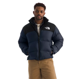 A man wearing a navy blue and black puffer jacket with a white embroidered The North Face logo on the chest, paired with tan pants, against a solid white background. - The North Face 1996 Retro Nuptse Jacket (Men's) - Summit Navy/TNF Black