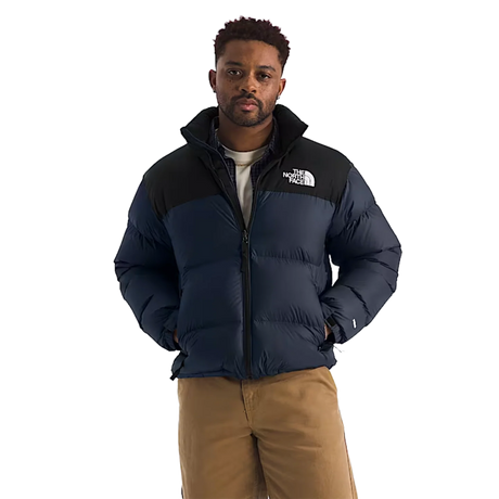 A man wearing a navy blue and black puffer jacket with a white embroidered The North Face logo on the chest, paired with tan pants, against a solid white background. - The North Face 1996 Retro Nuptse Jacket (Men's) - Summit Navy/TNF Black