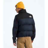 Person wearing a black and blue puffer jacket with 'The North Face' logo, yellow beanie, and beige pants on a white background. - The North Face 1996 Retro Nuptse Vest (Men's) - Summit Navy/TNF Black-Recycled Down