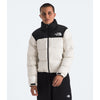 A model wearing a black and off-white puffer jacket by The North Face, paired with black sweatpants, against a light gray studio background. - The North Face 1996 Retro Nuptse Jacket (Womens) - White Dune/TNF Black-Recycled Down