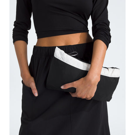 Person wearing black pants with a white stripe, holding a black bag. - The North Face 1996 Retro Nuptse Vest (Womens) - White Dune/TNF Black-Recycled Down