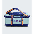 A light blue and navy duffel bag with bright orange straps and accents, featuring multiple brand patches on the front, set against a light gray background. - The North Face Base Camp Duffel Small 50L - Canal Blue/Bold Blue/Papaya