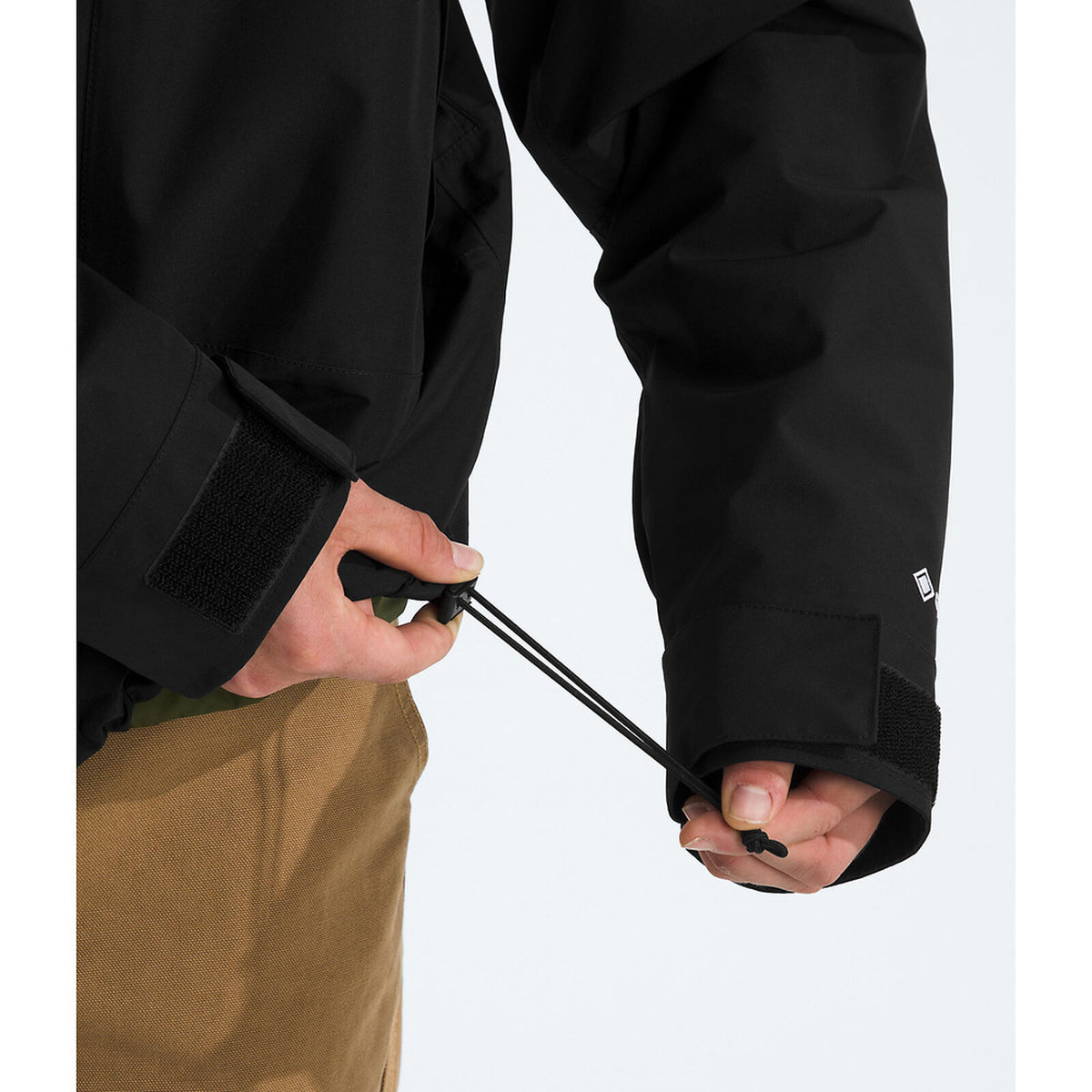 Person wearing a black jacket with a visible brand logo, holding a black cord. - The North Face GORE-TEX Mountain Jacket (Men's) - TNF Black/TNF Black/TNF Black
