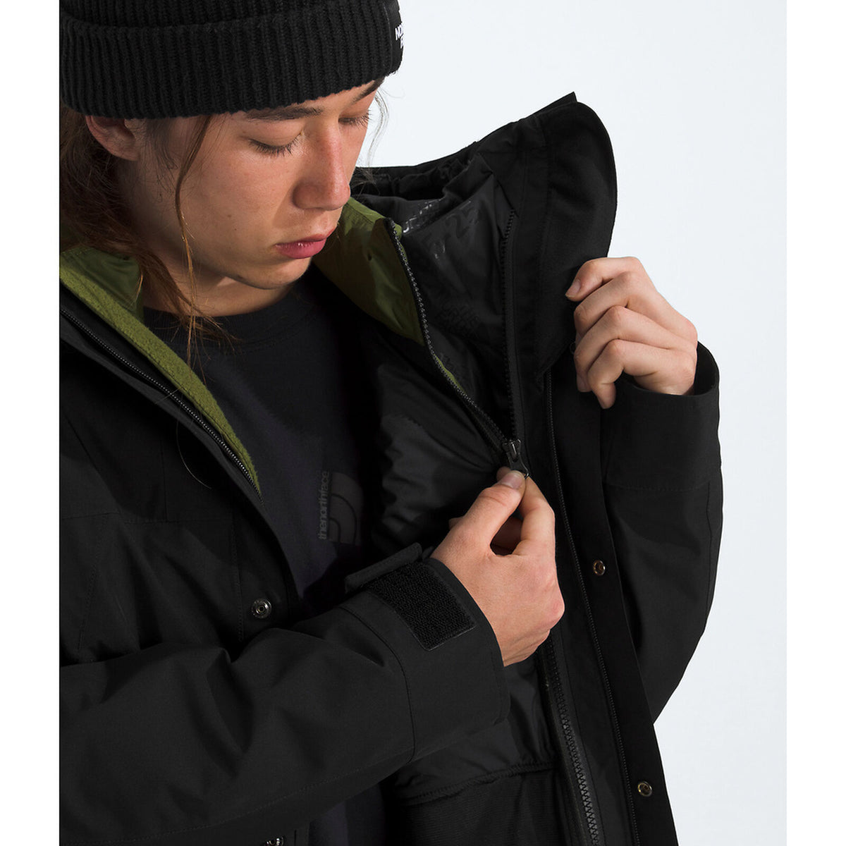 Person wearing a black jacket with a hood, adjusting it on a white background - The North Face GORE-TEX Mountain Jacket (Men's) - TNF Black/TNF Black/TNF Black