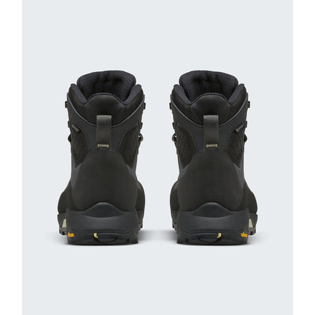 A pair of black high-top hiking boots shown from the back, featuring a matte finish with small gold accents on the pull tabs and outsole. - The North Face Verto Alpine Mid GORE-TEX Boots (Women's) - Anthracite Grey/Lemon Mist