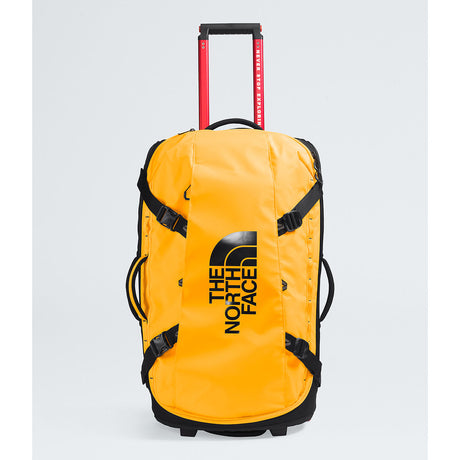 The North Face yellow rolling duffel bag with black straps, a black logo, and a red telescoping handle on a light gray background. - The North Face Base Camp Rolling Thunder 28" (95L) - Summit Gold/TNF Gold-NPF