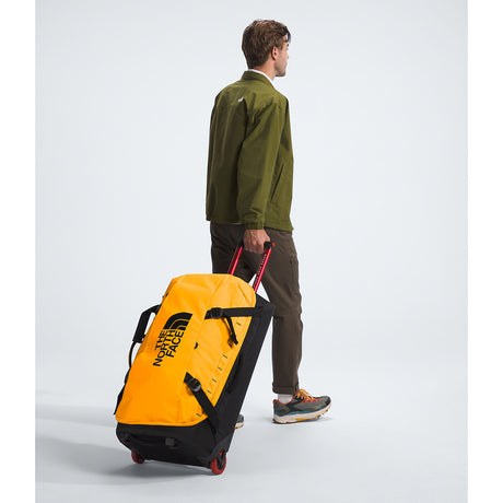 Person pulling a yellow and black North Face suitcase on a white background - The North Face Base Camp Rolling Thunder 28" (95L) - Summit Gold/TNF Gold-NPF