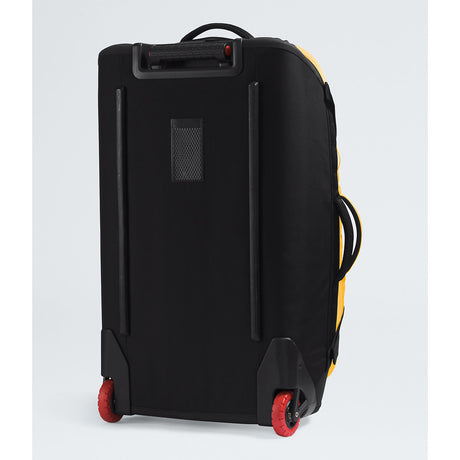 A black soft-sided rolling suitcase with red wheels, shown from a rear three-quarter angle against a light gray studio background. - The North Face Base Camp Rolling Thunder 28" (95L) - Summit Gold/TNF Gold-NPF
