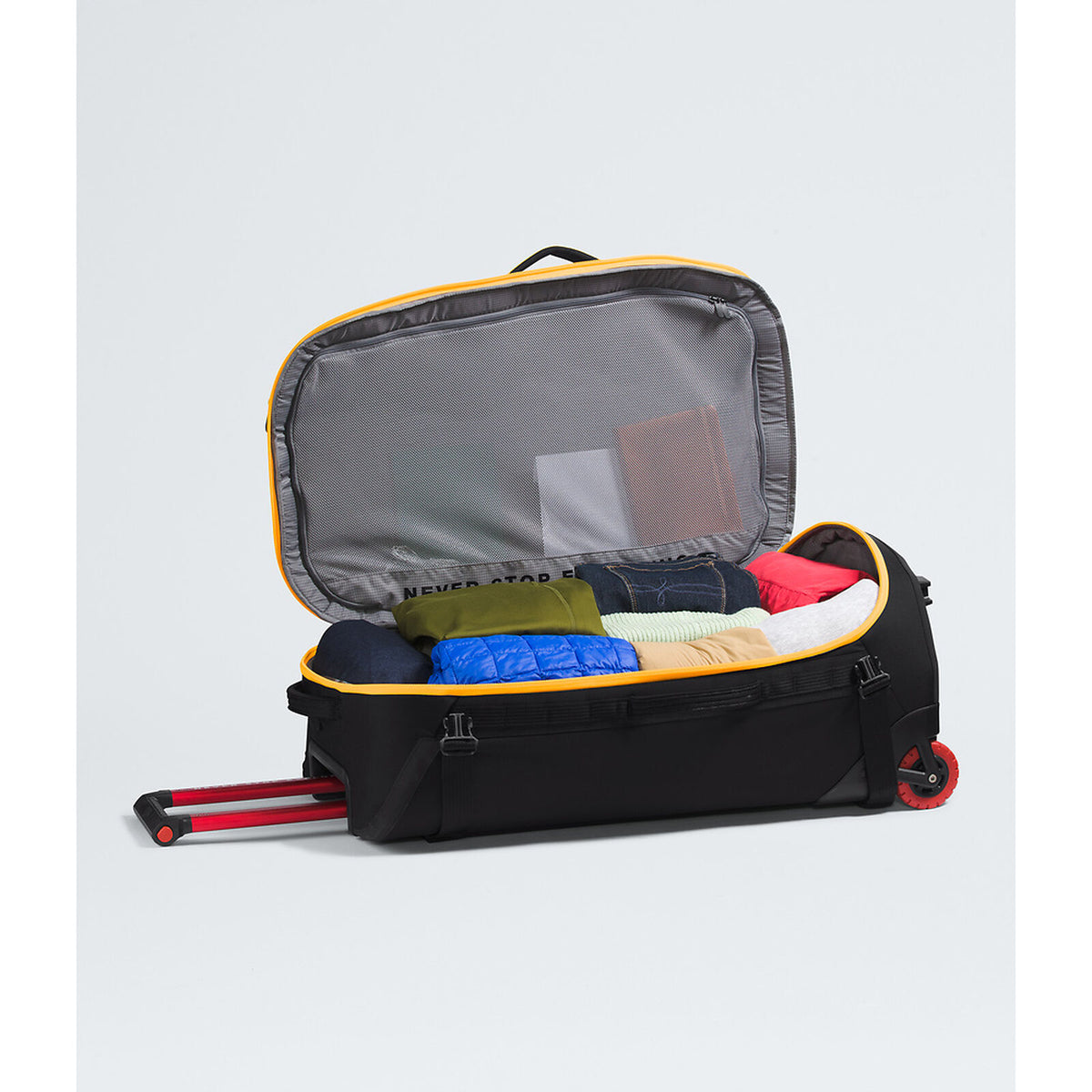 An open black rolling suitcase with yellow trim, shown with its telescoping handle extended and packed with folded clothes inside, on a light gray studio background. - The North Face Base Camp Rolling Thunder 28" (95L) - Summit Gold/TNF Gold-NPF