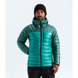 A man wearing a teal green puffer jacket with a high collar, black beanie, and black pants, standing against a light gray studio background. The small white 'THE NORTH FACE' logo is visible on the left chest of the jacket. -  - The North Face Summit Series Breithorn Hoodie (Men's) - Restorative Teal/Pacific Teal