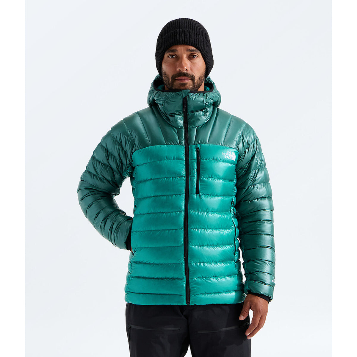 A man wearing a teal green puffer jacket with a high collar, black beanie, and black pants, standing against a light gray studio background. The small white 'THE NORTH FACE' logo is visible on the left chest of the jacket. -  - The North Face Summit Series Breithorn Hoodie (Men's) - Restorative Teal/Pacific Teal
