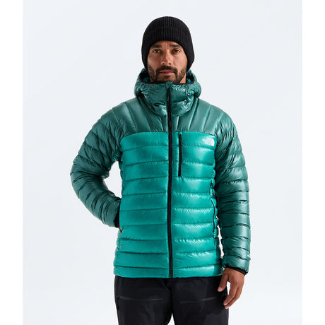 A man wearing a teal green puffer jacket with a high collar, black beanie, and black pants, standing against a light gray studio background. The small white 'THE NORTH FACE' logo is visible on the left chest of the jacket. -  - The North Face Summit Series Breithorn Hoodie (Men's) - Restorative Teal/Pacific Teal