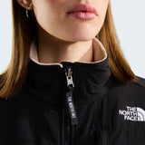 Close-up of a person wearing a black The North Face puffer jacket with a fleece-lined collar and a white embroidered logo on the chest. - The North Face Retro Denali Fleece Jacket (Women's) - Timeless Taupe/TNF Black
