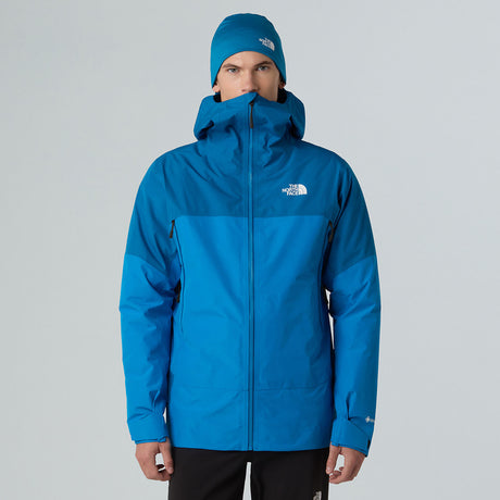 Person wearing a blue jacket and hat with The North Face logo on a gray background - The North Face Jazzi 3L GORE-TEX Jacket (Men's) - Skyline Blue/Adriatic Blue