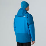 Person wearing a blue jacket and beanie with a visible brand logo on a gray background - The North Face Jazzi 3L GORE-TEX Jacket (Men's) - Skyline Blue/Adriatic Blue