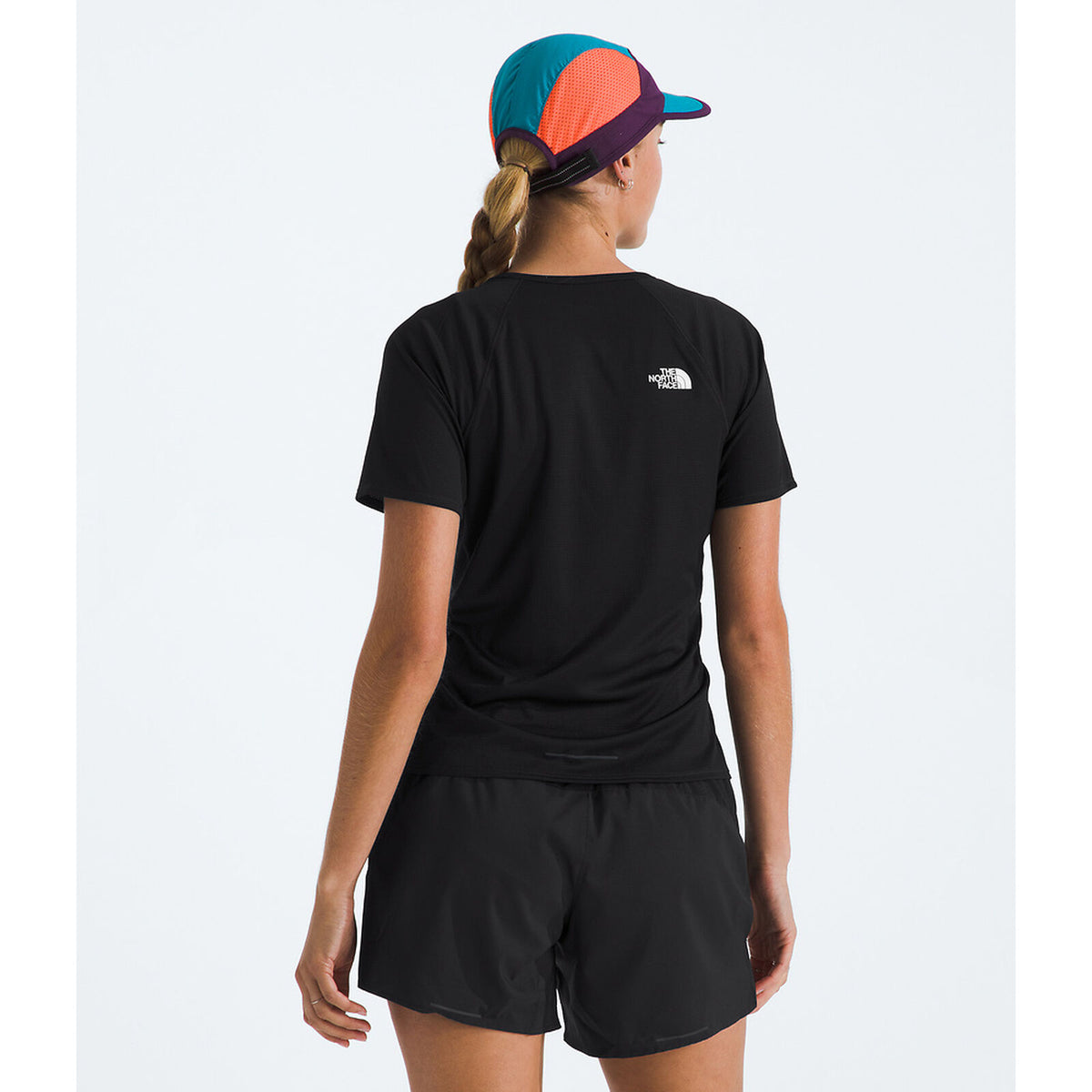 A woman shown from the back wearing a black short-sleeve athletic T-shirt with a small white The North Face logo on the upper back, black shorts, and a multicolor cap against a light gray studio background. - The North Face Sunriser Short-Sleeve T-Shirt (Women's) - TNF Black