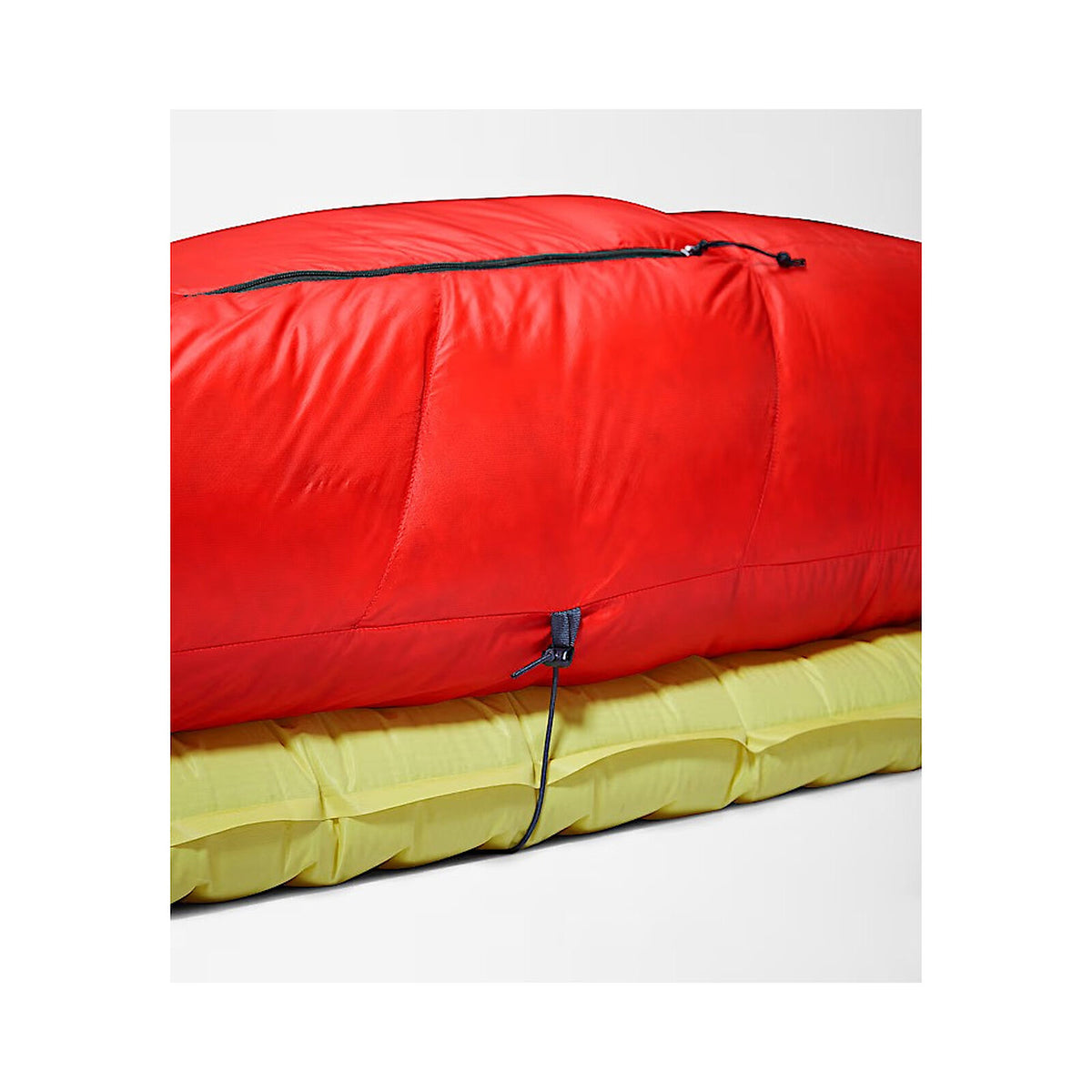 A bright red sleeping bag or padded sleeping pad shown folded and stacked on top of a yellow padded item, photographed on a clean light gray studio background. - The North Face Inferno Sleeping Bag - 20F / -29C