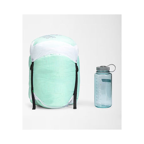 A mint green and white backpack shown next to a translucent blue water bottle with a gray cap, set against a plain light gray background. - The North Face Inferno Sleeping Bag - 0F / -18C