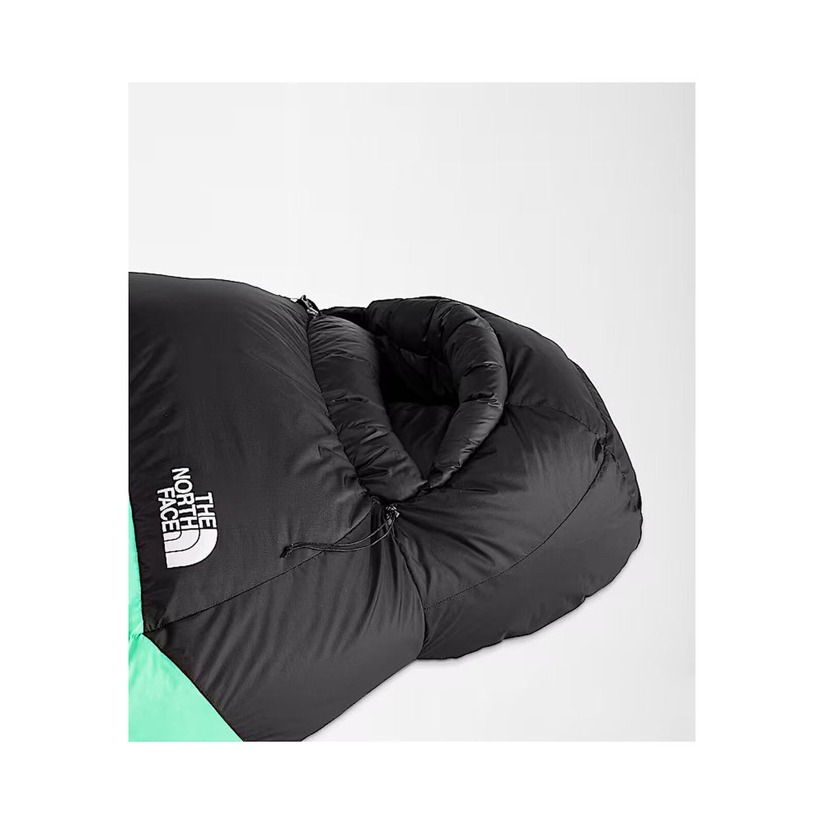 A close-up of a black sleeping bag with a white The North Face logo on the side, showing a mint green section at the bottom, set against a light gray background. - The North Face Inferno Sleeping Bag - 0F / -18C
