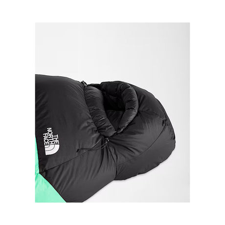 A close-up of a black sleeping bag with a white The North Face logo on the side, showing a mint green section at the bottom, set against a light gray background. - The North Face Inferno Sleeping Bag - 0F / -18C