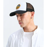 A man wearing a black and white trucker hat with a circular embroidered logo on the front, paired with a white button-down shirt, photographed against a clean white background. - The North Face Graphic Mudder Trucker - TNF White/TNF Black/TNF NSE Dome Patch
