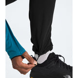 A close-up of a person's leg and hand adjusting the elastic cuff of black pants, wearing a white sock and a black The North Face running shoe. - The North Face Summit Summit Series Off Width Pants (Men's) - TNF Black