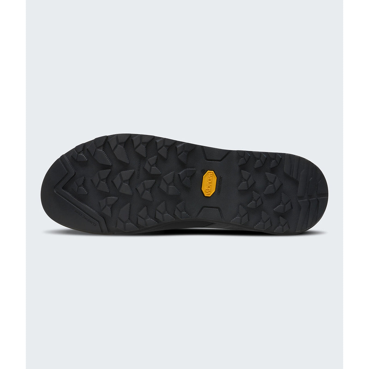 A close-up view of a black hiking shoe sole with a textured tread pattern and a small yellow Vibram logo in the center, set against a light gray background. - The North Face Verto Approach Shoes (Unisex) - Smoked Pearl/TNF Black