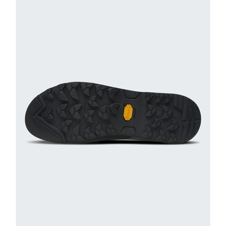 A close-up view of a black hiking shoe sole with a textured tread pattern and a small yellow Vibram logo in the center, set against a light gray background. - The North Face Verto Approach Shoes (Unisex) - Smoked Pearl/TNF Black