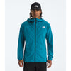 A man wearing a teal blue hooded jacket by The North Face, paired with a black beanie and black pants, standing against a light gray studio background. - The North Face Summit Series Off Width Jacket (Men's) - Dusk Blue
