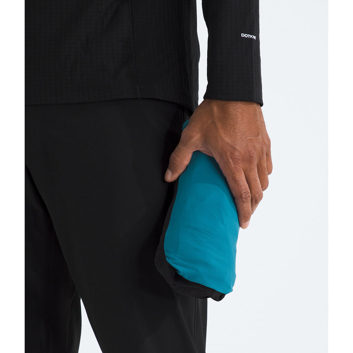 A close-up of a person wearing black athletic apparel and holding a compact, bright turquoise-blue running jacket or sleeve in one hand against a clean white background. - The North Face Summit Series Off Width Jacket (Men's) - Dusk Blue