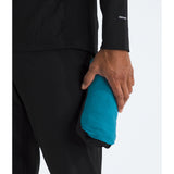 A close-up of a person wearing black athletic apparel and holding a compact, bright turquoise-blue running jacket or sleeve in one hand against a clean white background. - The North Face Summit Series Off Width Jacket (Men's) - Dusk Blue