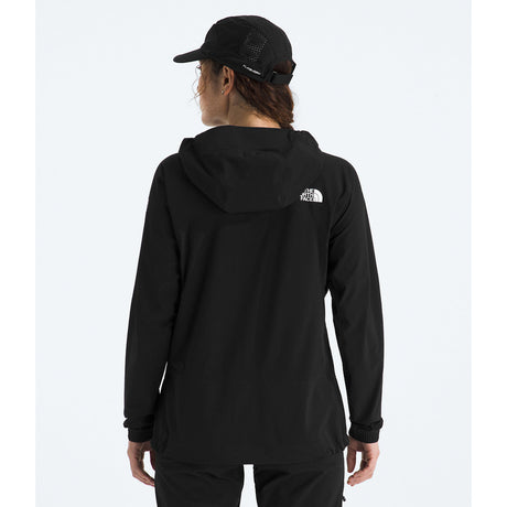 A woman viewed from behind wearing a black hooded jacket with a small white The North Face logo on the back, along with a black cap, against a light gray studio background. - The North Face Summit Series Off Width Jacket (Women's) - TNF Black