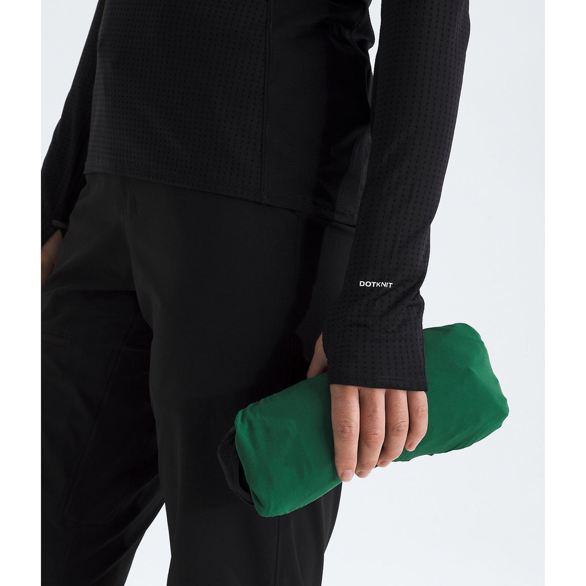 A close-up of a person wearing black textured athletic apparel and holding a compact, rolled green item in one hand against a clean white background. The sleeve shows the visible brand name The North Face. - The North Face Summit Series Off Width Jacket (Women's) - Evergreen