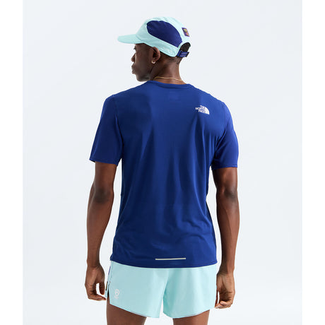 A man wearing a royal blue short-sleeve athletic t-shirt from the back, paired with light blue shorts and a matching light blue and navy cap, against a plain white background. - The North Face Summit High Trail Short Sleeve-Graphic (Men's) - Bold Blue
